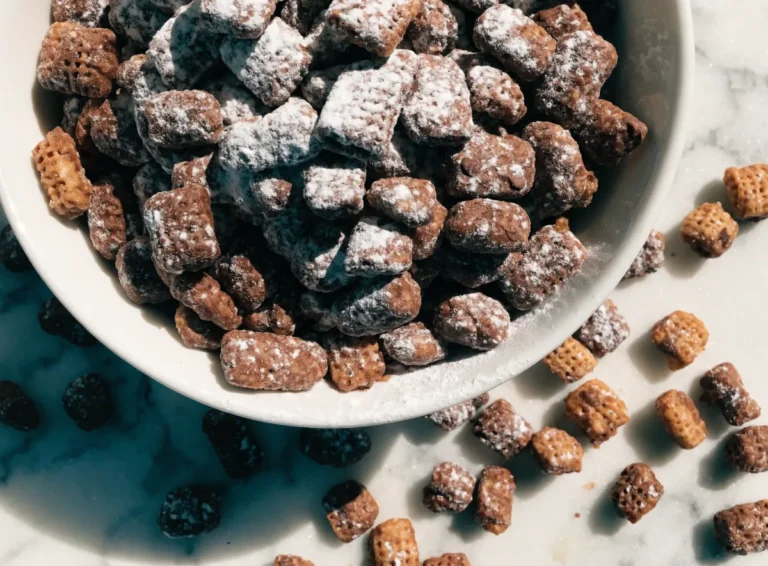 Puppy chow coated in chocolate and powdered sugar in a white bowl